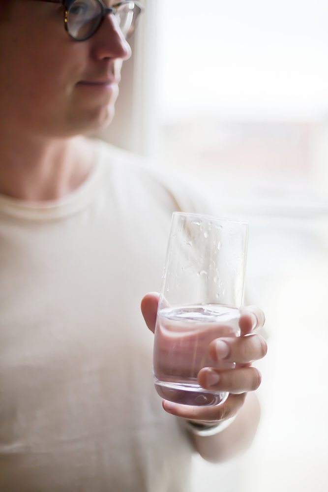 Man i glasögon med vattenglas i handen vid fönster